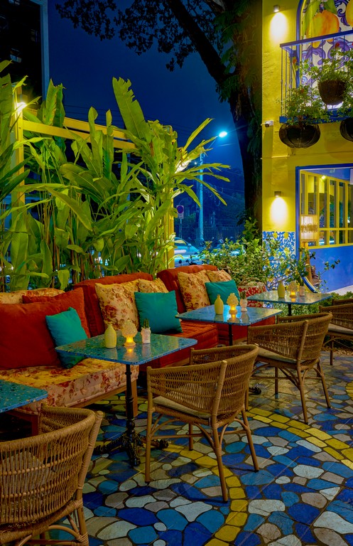 Outdoor sofa seating with red and teal cushions, rattan chairs and blue mosaic paving on the Mandorla garden terrace at night