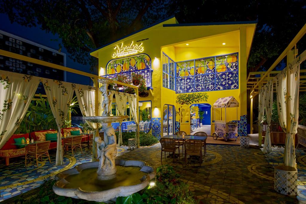 Mandorla Sicilian Bistrot at night, the yellow house behind its garden terrace with a fountain and curtained pergolas in Nimman, Chiang Mai
