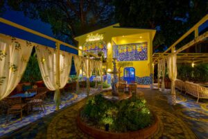 Mandorla Sicilian Bistrot at night, the yellow house lit up behind a garden terrace with a stone fountain and curtained pergolas in Nimman, Chiang Mai