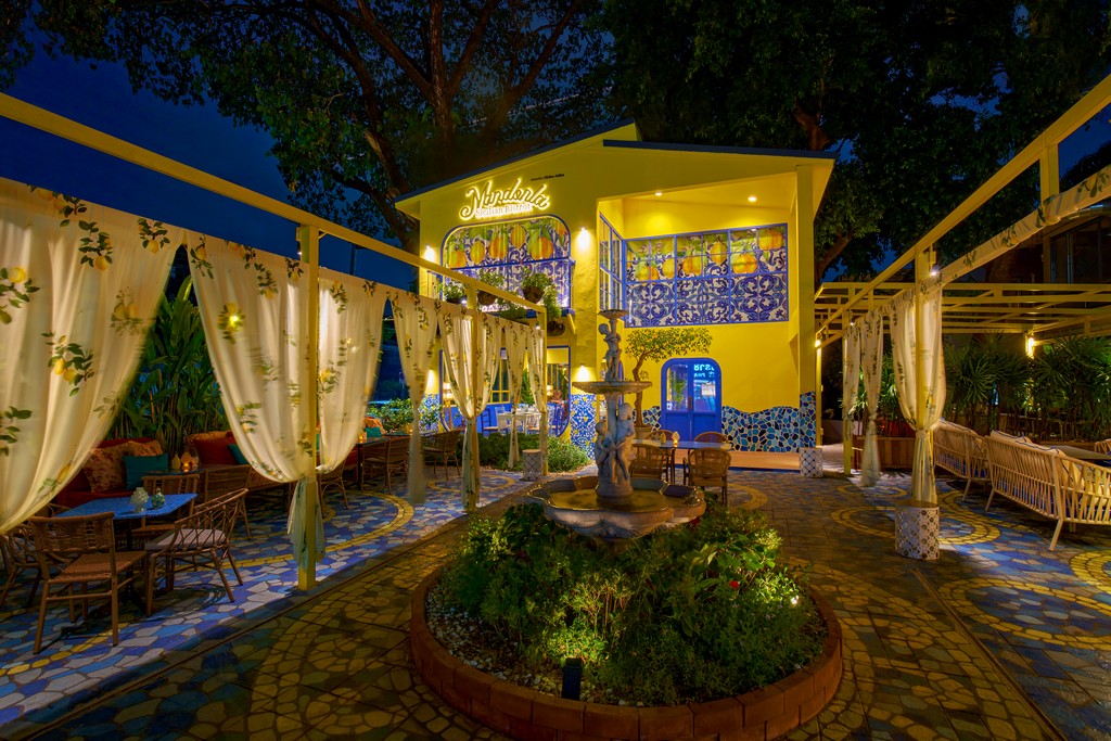 Mandorla Sicilian Bistrot at night, the yellow house lit up behind a garden terrace with a stone fountain and curtained pergolas in Nimman, Chiang Mai