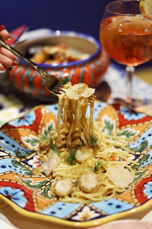 Seafood spaghetti twirled on a fork over a hand painted Sicilian plate, with an Aperol Spritz behind, at Mandorla, Chiang Mai